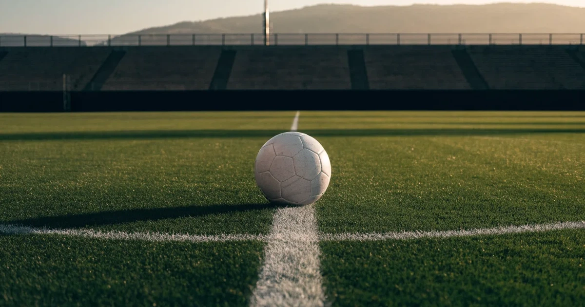 Ein Fussball liegt auf dem Mittelkreis eines Rasenfelds, die weissen Linien kreuzen sich auf dem gepflegten Gras im warmen Abendlicht.
