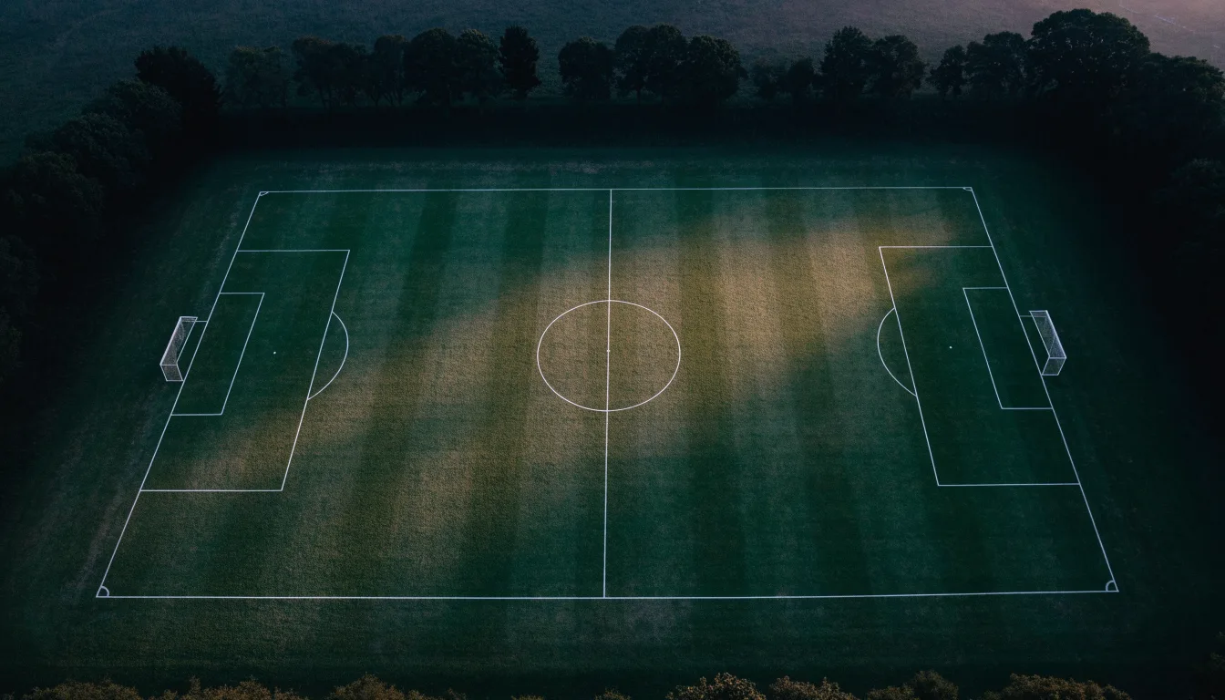 Ein Fussballplatz von oben gesehen, die Linien bilden ein helles Muster auf dem Rasen, Drohnenperspektive in der Morgendämmerung.