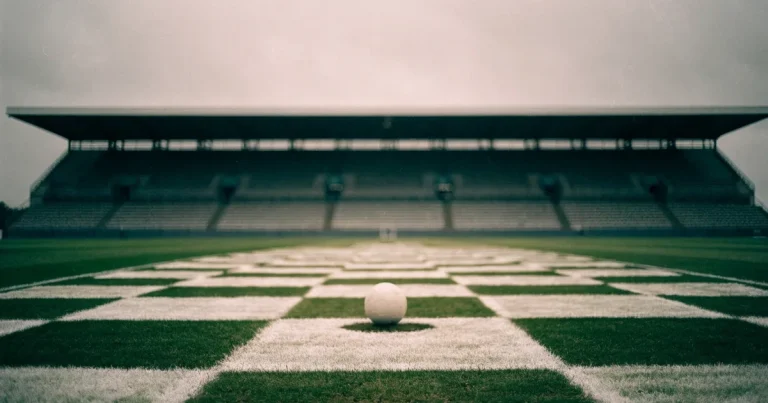 Ein Fussball liegt auf dem Anstosspunkt eines frisch gemähten Rasens, dahinter eine grosse Tribüne unter bewölktem Himmel