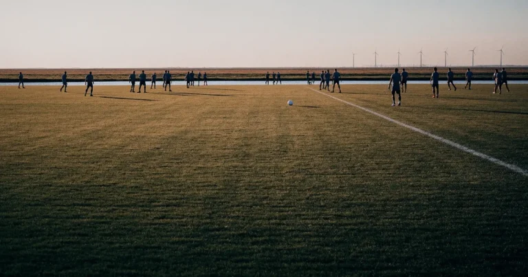 Ein Fussballplatz neben einem Kanal in flachem Land mit Windrädern am Horizont, Abendlicht liegt über dem Rasen